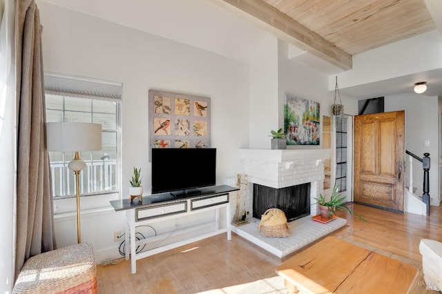 living area with a brick fireplace, beam ceiling, and wood finished floors