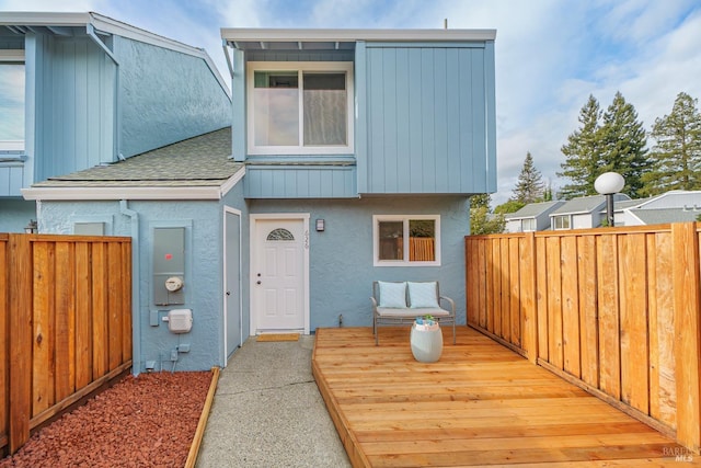 view of front of house with a shingled roof, fence, and stucco siding