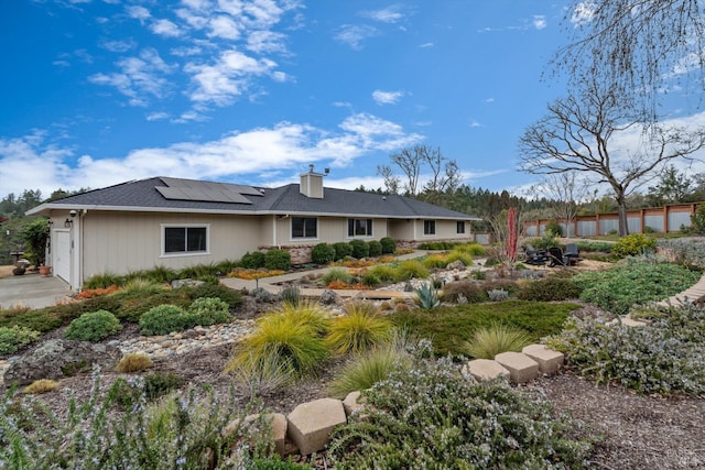 back of property featuring an attached garage, a chimney, fence, and solar panels