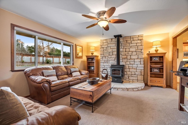 living area with a wood stove, carpet, and a ceiling fan