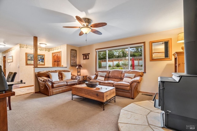 living area with visible vents, a ceiling fan, a wood stove, light carpet, and baseboards