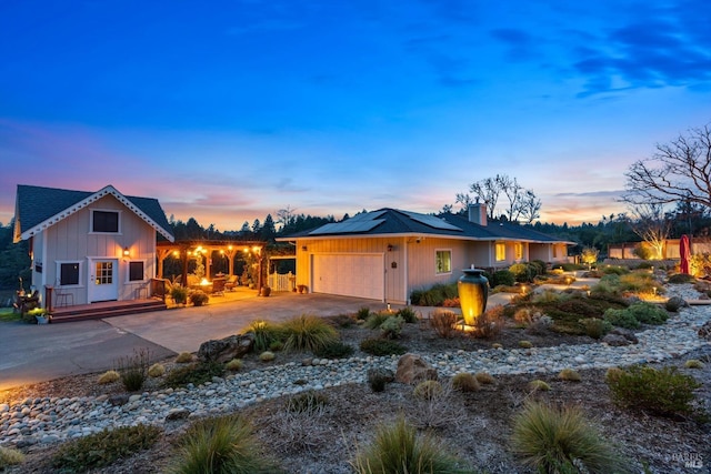 view of front of home featuring a deck, an attached garage, solar panels, concrete driveway, and a chimney