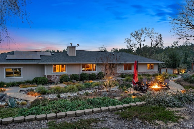 back of property at dusk with an outdoor fire pit, roof mounted solar panels, and a chimney