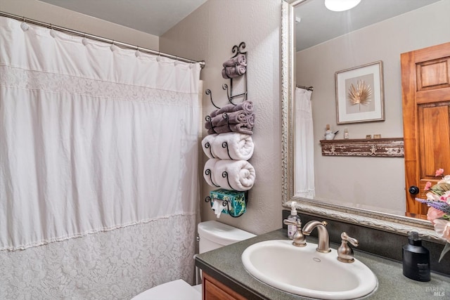 bathroom with a shower with curtain, a textured wall, vanity, and toilet