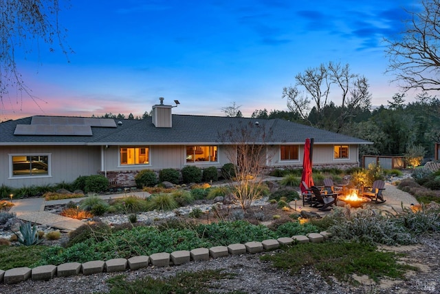 4630 Maddocks Rd, Sebastopol, CA 95472 - back of house at dusk with an outdoor fire pit, a chimney, roof mounted solar panels, a shingled roof, and a patio