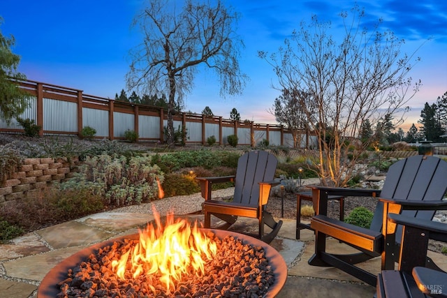 patio terrace at dusk featuring an outdoor fire pit and a fenced backyard