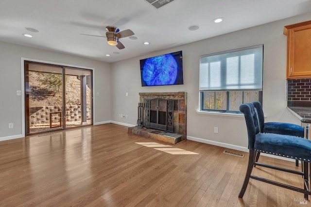 living area featuring a stone fireplace, baseboards, visible vents, and light wood finished floors