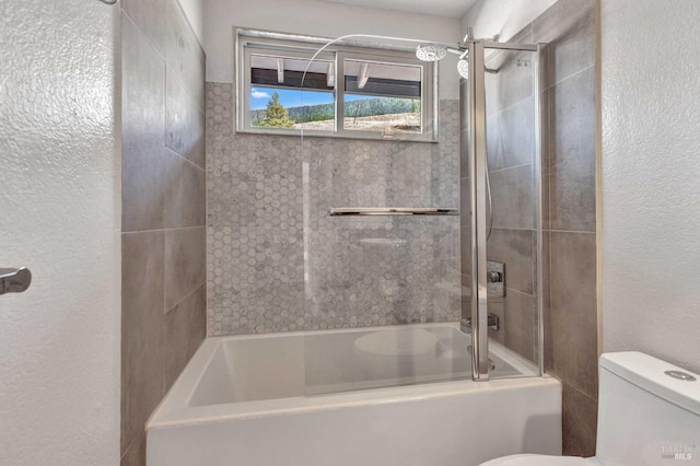 bathroom with toilet, a textured wall, and shower / bath combination with glass door