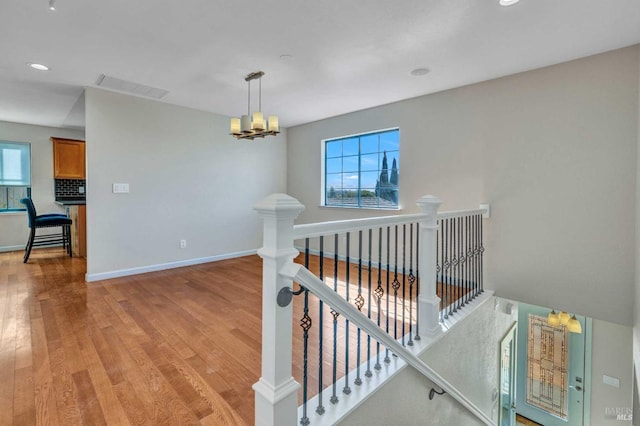 hall with visible vents, baseboards, an upstairs landing, light wood-style floors, and a notable chandelier