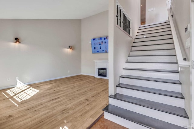 stairway featuring a glass covered fireplace, wood finished floors, and baseboards