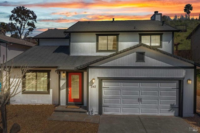 traditional-style house featuring driveway, a chimney, an attached garage, and a shingled roof