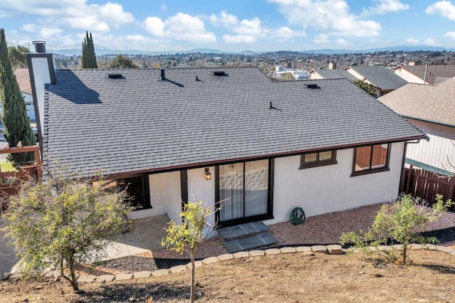 back of house with fence, a chimney, and a shingled roof