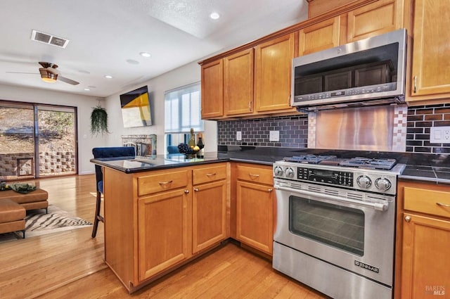 kitchen featuring stainless steel appliances, a peninsula, visible vents, and light wood-style flooring