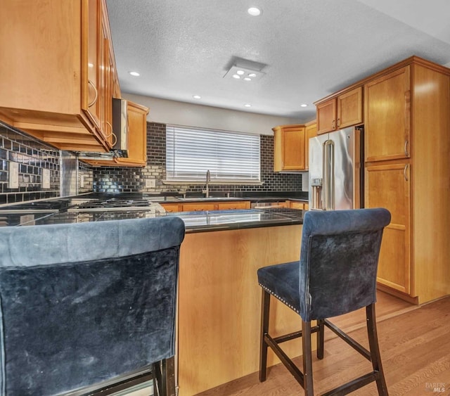 kitchen with a kitchen bar, a sink, dark countertops, light wood-style floors, and high end refrigerator