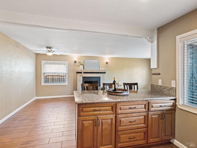 kitchen with a peninsula, light stone counters, a fireplace, and baseboards