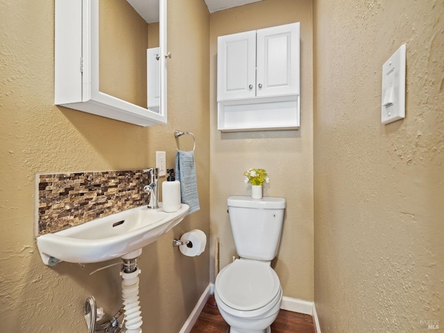 half bath featuring toilet, a sink, wood finished floors, baseboards, and decorative backsplash