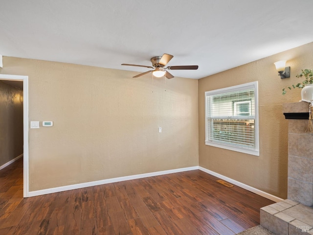 empty room with a tile fireplace, visible vents, baseboards, and wood finished floors