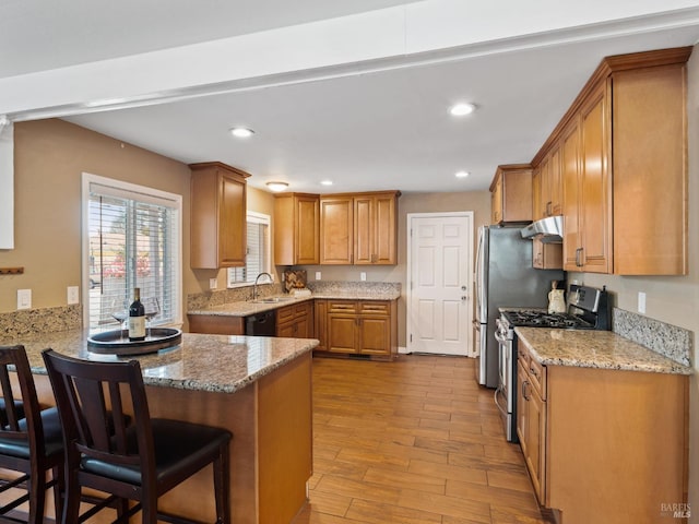 kitchen featuring brown cabinetry, gas range, a peninsula, under cabinet range hood, and a sink