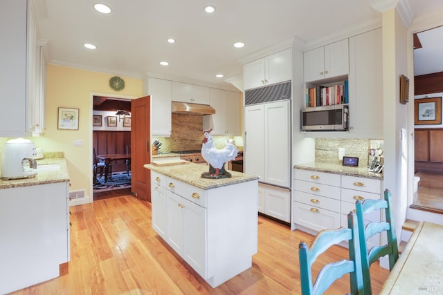 kitchen with white cabinets, stainless steel microwave, a center island, light wood-type flooring, and under cabinet range hood