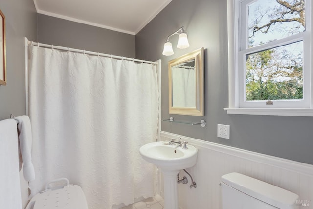 full bath featuring toilet, a shower with shower curtain, a sink, wainscoting, and crown molding