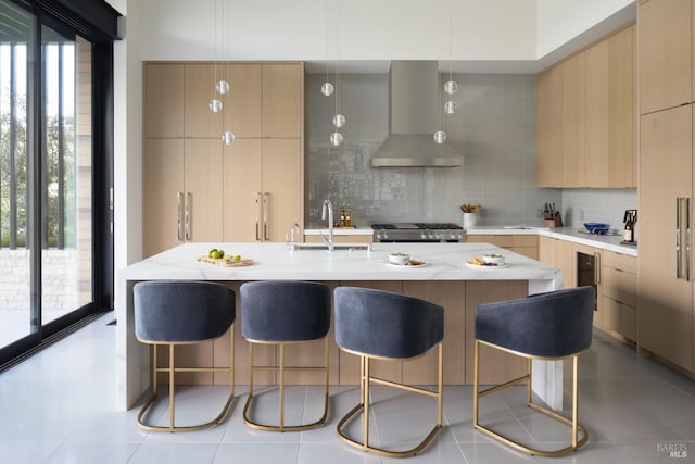 kitchen featuring wall chimney range hood, modern cabinets, a sink, and decorative backsplash