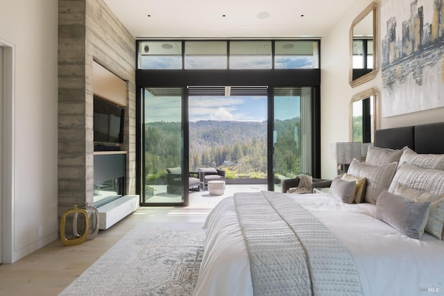 bedroom featuring access to outside, a high ceiling, expansive windows, and wood finished floors