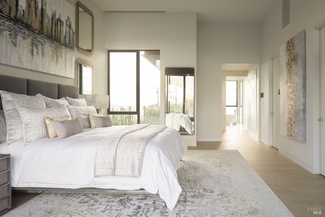 bedroom featuring baseboards, a high ceiling, visible vents, and light wood-style floors