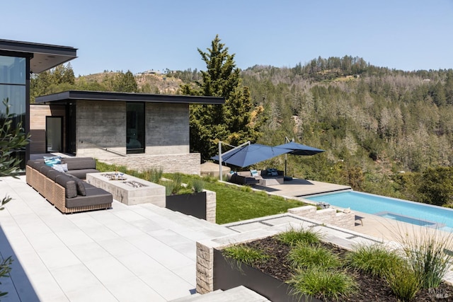 view of patio with a forest view, an outdoor pool, and an outdoor living space with a fire pit