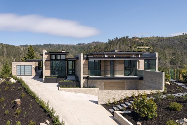 modern home with a garage, driveway, a balcony, and a wooded view