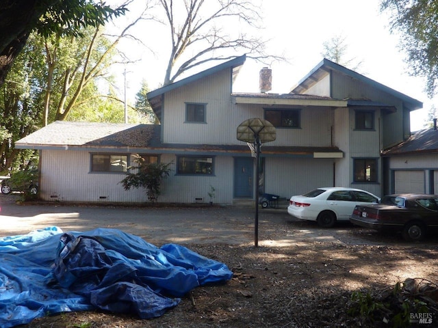 view of front facade with dirt driveway, crawl space, a chimney, and an attached garage