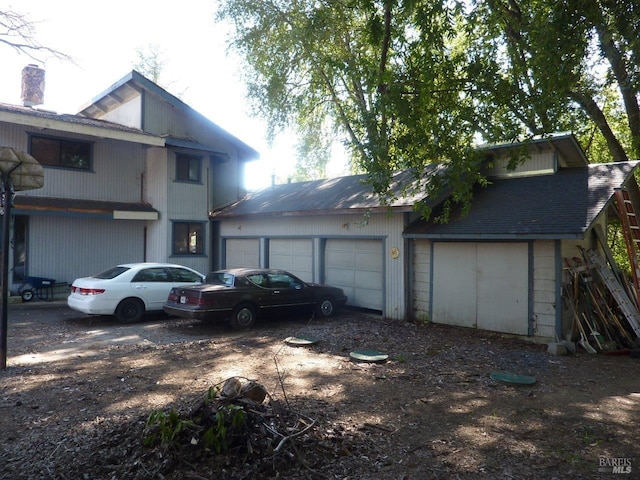 view of front of home featuring driveway, a shingled roof, a garage, and a chimney