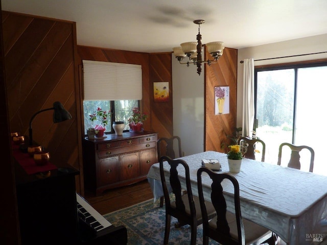 dining room featuring a notable chandelier, dark wood finished floors, and wooden walls