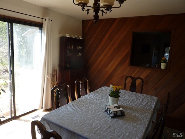 dining room featuring wooden walls, plenty of natural light, visible vents, and a notable chandelier