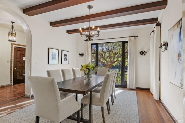 dining area featuring arched walkways, a notable chandelier, light wood-style floors, baseboards, and beam ceiling