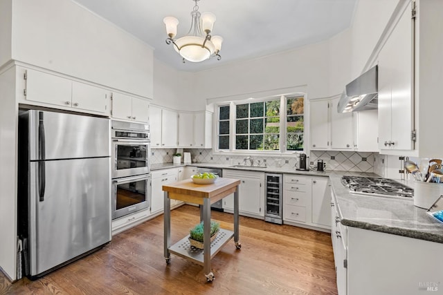 kitchen with decorative backsplash, appliances with stainless steel finishes, a sink, beverage cooler, and wall chimney exhaust hood