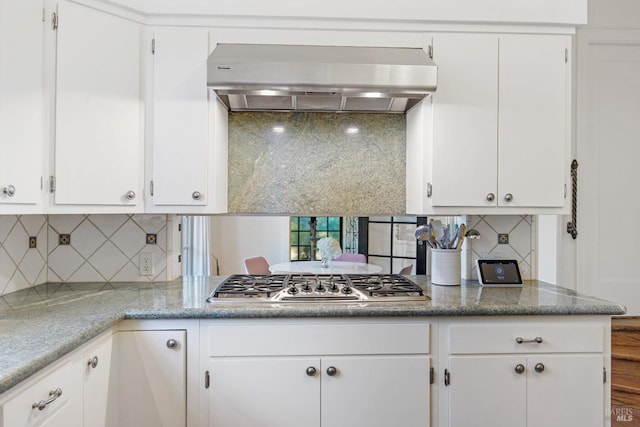 kitchen featuring white cabinets, wall chimney exhaust hood, light stone counters, stainless steel gas stovetop, and backsplash