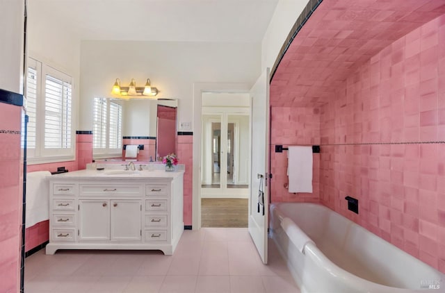 bathroom featuring a wainscoted wall, tile walls, vanity, a tub, and tile patterned flooring