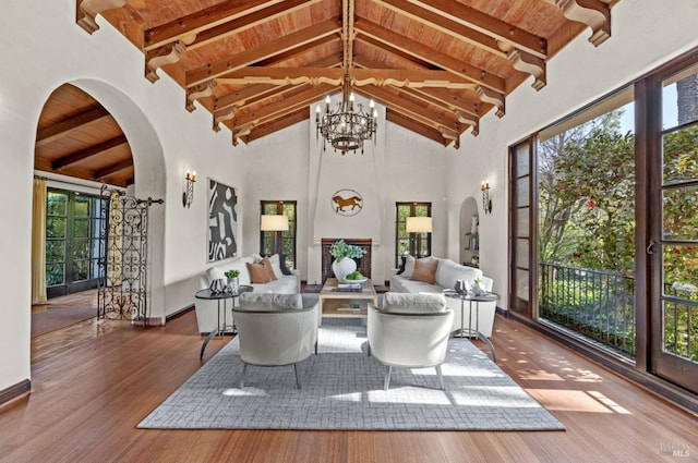 living area with arched walkways, wooden ceiling, beamed ceiling, wood finished floors, and a notable chandelier