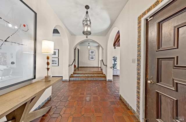 entryway featuring a chandelier, arched walkways, dark tile patterned flooring, baseboards, and stairway