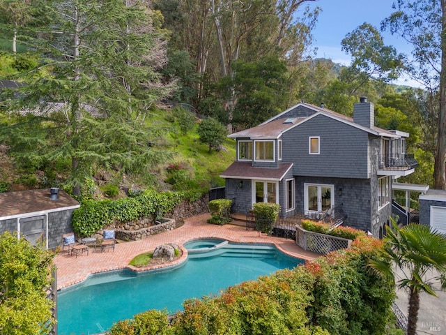 rear view of house with a chimney, a pool with connected hot tub, a patio area, fence, and a balcony