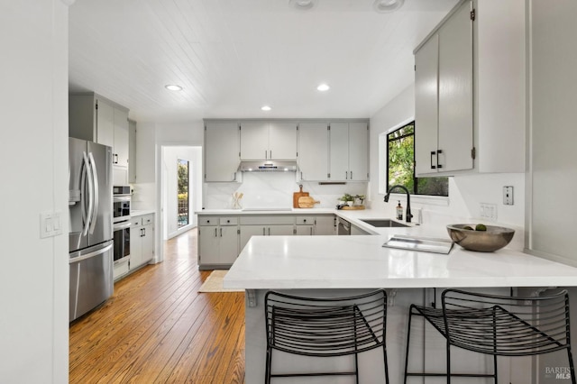 kitchen featuring gray cabinets, a sink, a peninsula, under cabinet range hood, and stainless steel fridge with ice dispenser