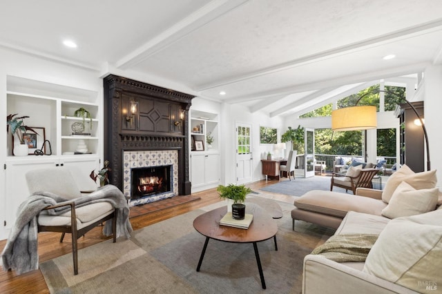 living room with lofted ceiling with beams, a tiled fireplace, built in features, and wood finished floors