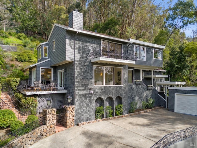 view of front of home with a balcony, a garage, concrete driveway, stairway, and a chimney