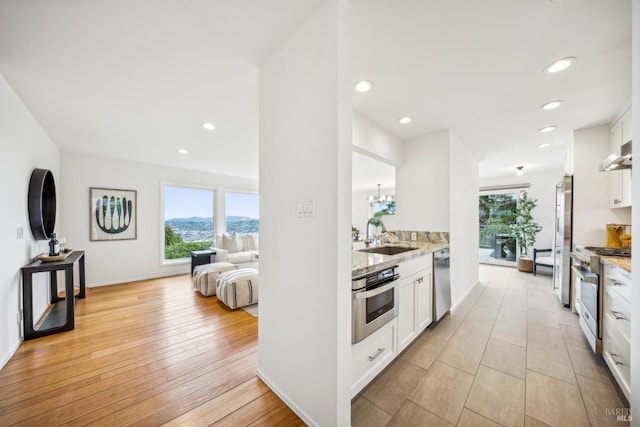 kitchen with open floor plan, white cabinetry, a sink, high quality appliances, and extractor fan