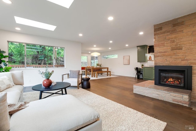 living room with a stone fireplace, dark wood-type flooring, a skylight, and recessed lighting