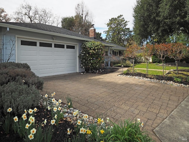 view of front of property with decorative driveway, a garage, and a chimney