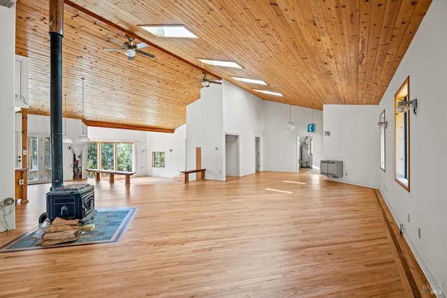 living area featuring light wood-type flooring, a skylight, a wood stove, and a ceiling fan