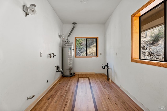 laundry area featuring light wood finished floors, water heater, and baseboards