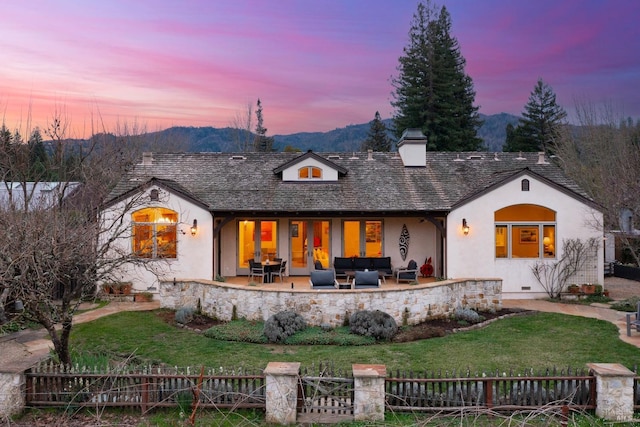 back of house at dusk featuring a chimney, stucco siding, a patio area, a mountain view, and fence private yard