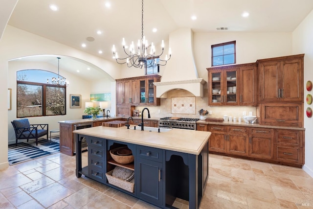 kitchen with brown cabinetry, custom exhaust hood, light countertops, stone tile flooring, and a chandelier